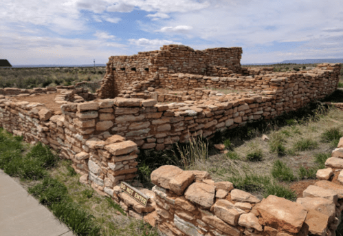 Ruins of an ancient stone structure surrounded by grass under a blue sky with scattered clouds.