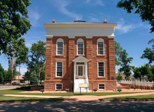 Historic brick building with a white entrance, surrounded by trees and a clear blue sky.