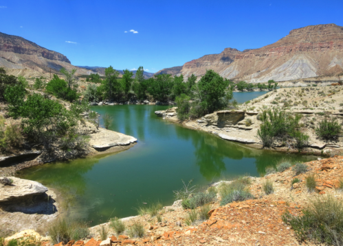 A serene landscape featuring a green river surrounded by rocky cliffs and lush trees under a clear blue sky.