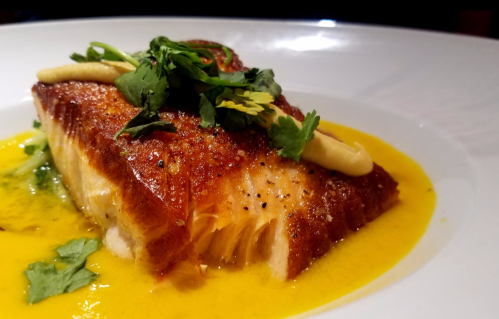 A beautifully plated piece of seared salmon topped with herbs and served in a vibrant yellow sauce.
