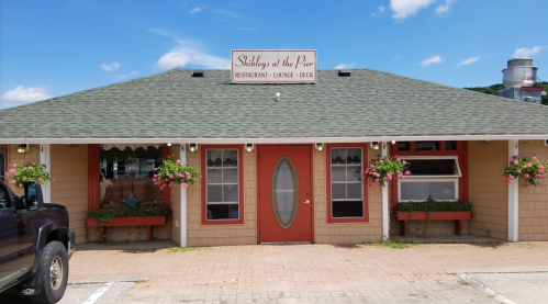 A cozy restaurant with a green roof and flower boxes, featuring a sign that reads "Shirley's at the Pier."