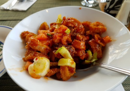A bowl of spicy shrimp stir-fry with vegetables, garnished with green onions and served with a spoon.