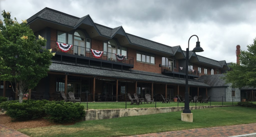 A brick building with a gray roof, featuring balconies and patriotic decorations, surrounded by green grass and trees.