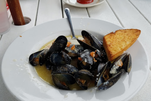 A plate of mussels in broth, garnished with herbs, accompanied by a slice of toasted bread.