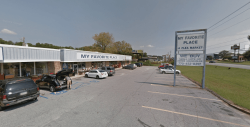 A view of a flea market with parked cars and a sign that reads "My Favorite Place" on a sunny day.