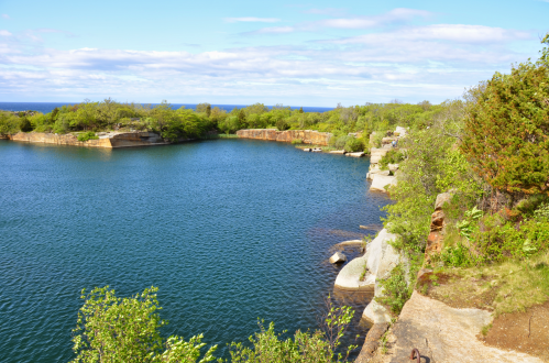 A serene lake surrounded by rocky shores and lush greenery under a blue sky with scattered clouds.