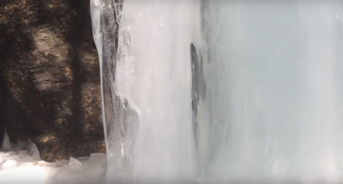 A close-up of ice formations with a rocky background, showcasing textures and light reflections.