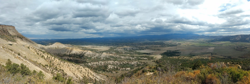 A panoramic view of a vast valley surrounded by mountains under a cloudy sky.