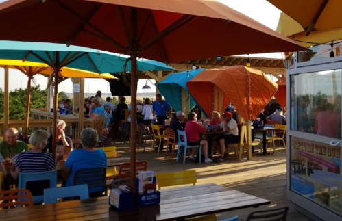 A vibrant outdoor dining area with colorful umbrellas, filled with people enjoying a meal on a sunny day.