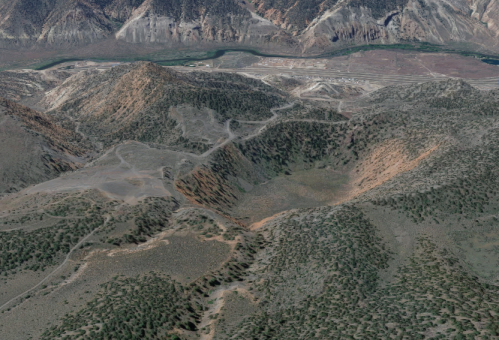Aerial view of rugged mountains and valleys with sparse vegetation and winding paths.