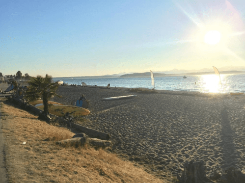 A serene beach scene at sunset, with a sandy shore, surfboards, and gentle waves under a clear sky.