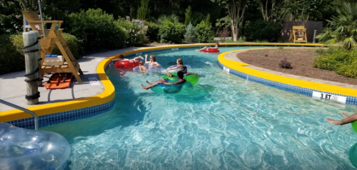People floating on colorful inner tubes in a winding lazy river surrounded by greenery and lounge chairs.