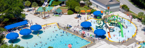 Aerial view of a vibrant water park with pools, slides, and colorful umbrellas, filled with people enjoying the sun.