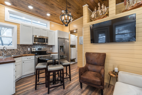 Cozy kitchen and living area with modern appliances, a dining table, and comfortable seating in warm wood tones.