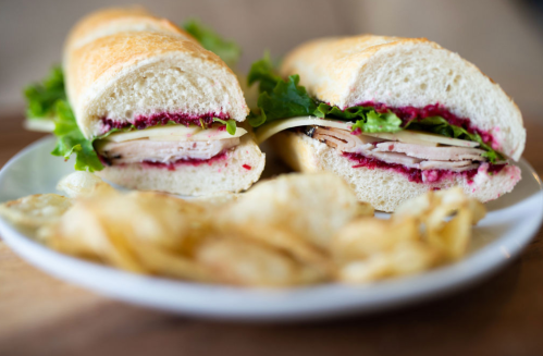 A close-up of a sandwich with turkey, lettuce, and cranberry sauce, served with a side of potato chips on a plate.