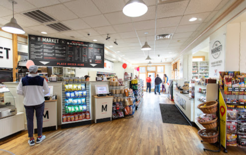 Interior of a market with a counter, snack displays, and customers browsing in a bright, spacious setting.