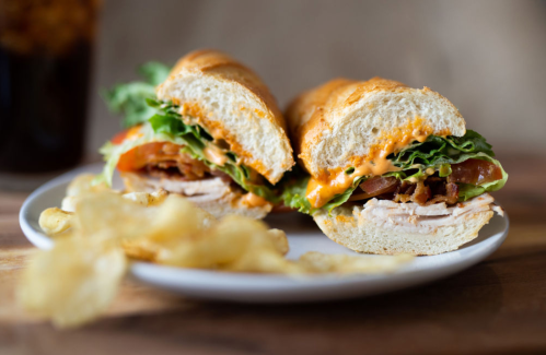 A close-up of a sandwich with turkey, lettuce, tomato, and cheese, served with a side of potato chips.