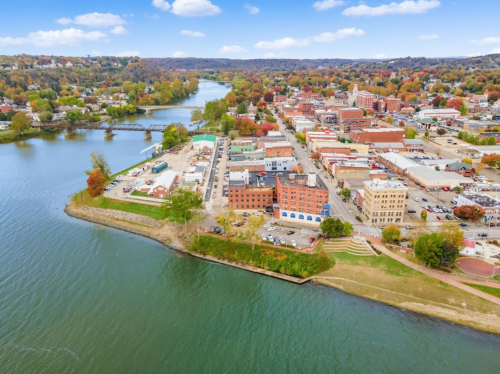 Aerial view of a riverside town with colorful autumn trees, buildings, and a bridge in the background.