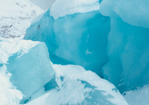 A close-up of bright blue ice formations with a snowy landscape in the background.
