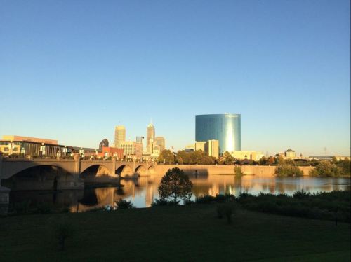 City skyline reflecting on a river, featuring modern buildings and a clear blue sky.