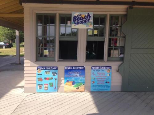 A beach shop with signs for items for sale, rental equipment, and sports equipment displayed outside.