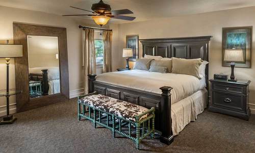 Cozy bedroom featuring a large bed, decorative bench, mirror, lamps, and warm lighting.