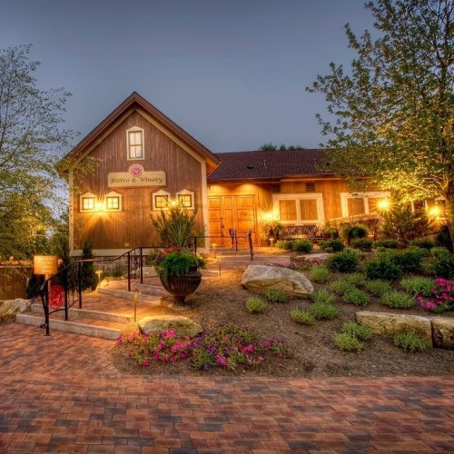 A charming winery building with warm lights, surrounded by landscaped gardens and colorful flowers at dusk.