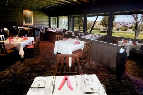 A cozy restaurant interior with wooden tables, white tablecloths, and pink napkins, overlooking a scenic view.