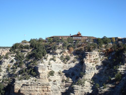 A lodge perched on a rocky cliff, surrounded by trees, against a clear blue sky.