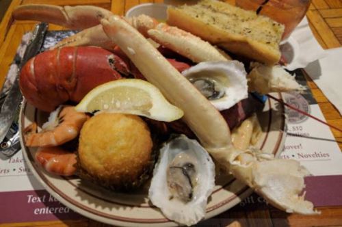 A seafood platter featuring lobster, shrimp, crab, oysters, a lemon wedge, cornbread, and garlic bread.