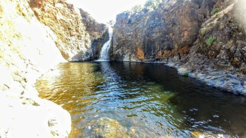 A serene waterfall cascading into a calm pool, surrounded by rocky cliffs and lush greenery.