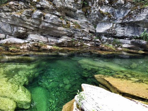 Clear green water flows over smooth rocks, surrounded by rugged cliffs and lush greenery.