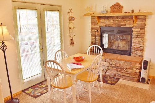 Cozy dining area with a wooden table, four chairs, a stone fireplace, and sliding glass doors. Warm and inviting atmosphere.