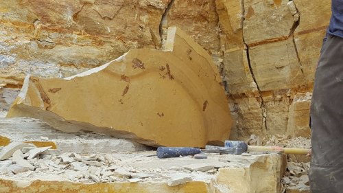A large, partially carved stone block in a quarry, with tools scattered around on the ground.