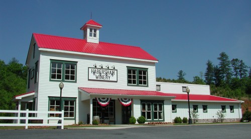 A white winery building with a red roof, featuring a sign that reads "Habersham Winery" and decorative bunting.