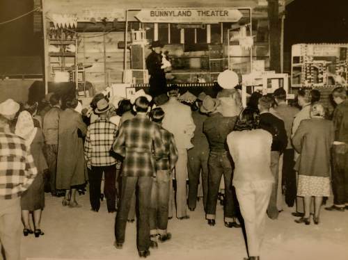 A crowd watches a performance at Bunnyland Theater, with a stage and colorful decorations in a vintage setting.