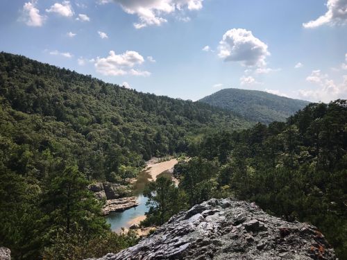 A scenic view of a river winding through lush green hills under a blue sky with fluffy clouds.