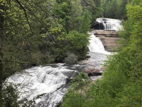 A scenic view of cascading waterfalls surrounded by lush green trees and rocky terrain.