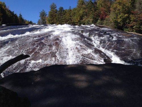 A cascading waterfall flows over a rocky surface, surrounded by trees in a vibrant autumn landscape.