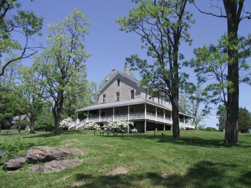 A large stone house surrounded by green trees and grass on a sunny day, with a porch and a clear blue sky.