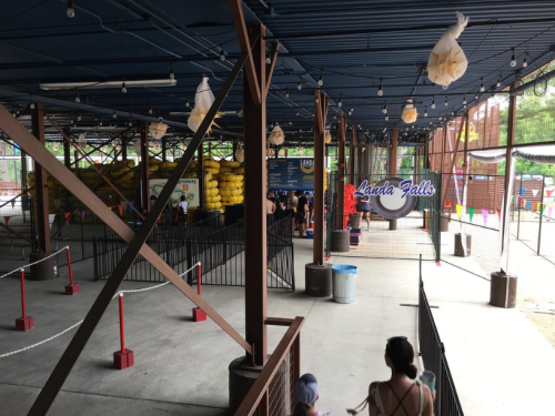 A spacious indoor area with a blue ceiling, featuring a line of people, colorful decorations, and a sign for "Landa Falls."