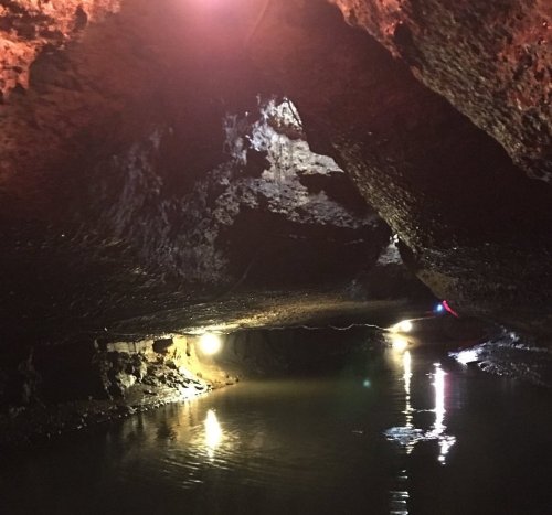 A dimly lit cave with rocky walls and a calm water surface reflecting lights.