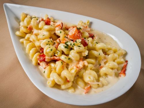 Creamy pasta with lobster, garnished with parsley, served in a white dish on a beige tablecloth.