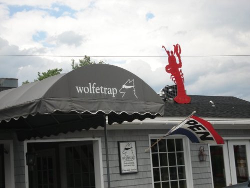 A restaurant with a gray awning labeled "wolftrap," featuring a red lobster sign and an "OPEN" flag.
