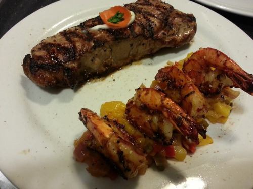 Grilled steak with a dollop of sauce, accompanied by seasoned shrimp and a colorful vegetable medley on a white plate.