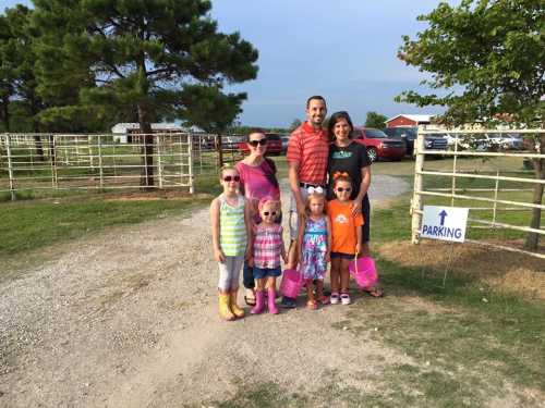 A family of six, including four children, poses together outdoors near a parking sign, smiling and wearing colorful outfits.