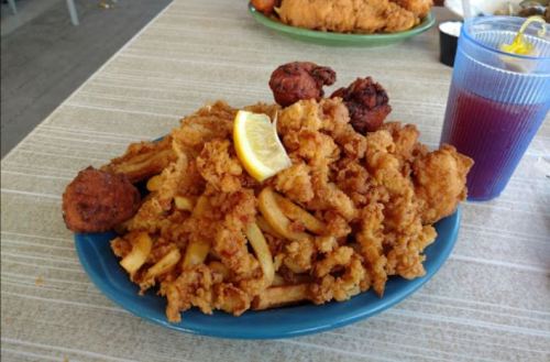 A blue plate piled high with fried chicken, French fries, and a lemon wedge, accompanied by a drink in a cup.