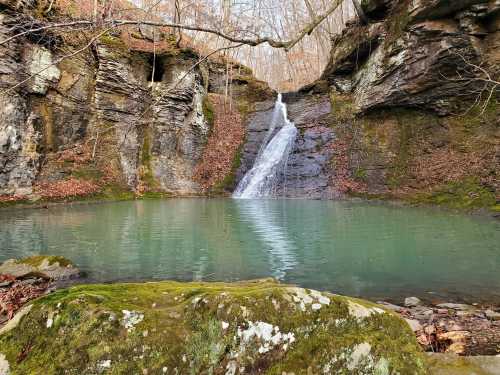 A serene waterfall cascades into a tranquil pool, surrounded by rocky cliffs and autumn foliage.