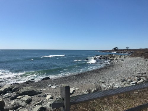A serene coastal view with gentle waves, rocky shore, and clear blue sky.