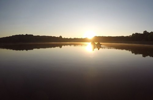 A serene sunrise over a calm lake, with a small boat silhouetted against the glowing horizon.
